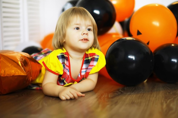 Porträt eines kleinen Kindes, das in einem mit Luftballons dekorierten Raum auf dem Boden liegt Glückliches Kindheitskonzept