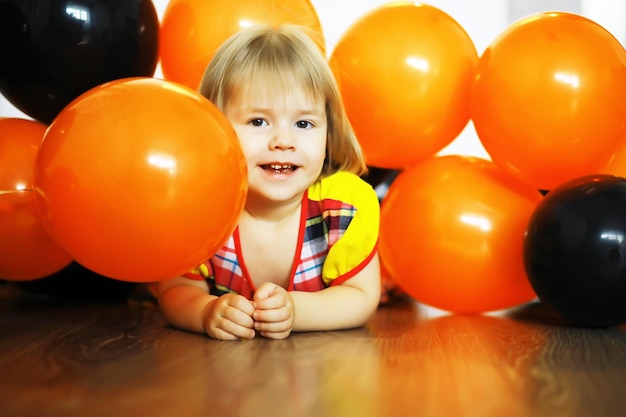 Porträt eines kleinen Kindes, das in einem mit Luftballons geschmückten Raum auf dem Boden liegt. Glückliches Kindheitskonzept.