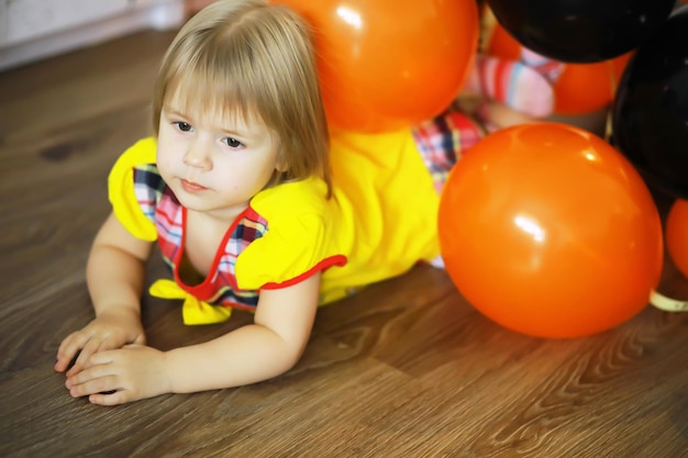 Porträt eines kleinen Kindes, das in einem mit Luftballons geschmückten Raum auf dem Boden liegt. Glückliches Kindheitskonzept.