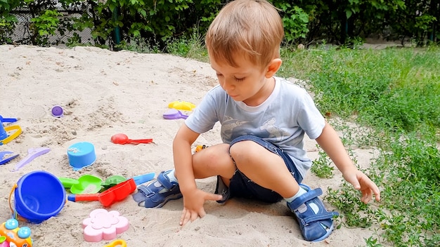 Porträt eines kleinen Kleinkindjungen, der mit Spielzeug spielt und Sand im Sandkasten im Park gräbt?