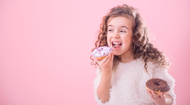 Porträt eines kleinen lockigen Mädchens, das Donuts isst