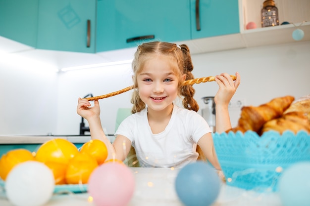 Porträt eines kleinen Mädchens 7 Jahre alt sitzt in der Küche und spielt mit Brotstangen. Kind frühstückt in der Küche