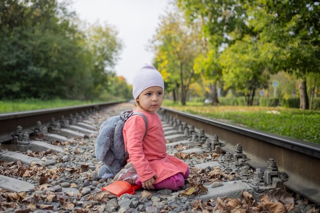 Porträt eines kleinen Mädchens, das auf den Bahngleisen im Wald sitzt