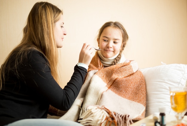 Porträt eines kleinen Mädchens, das sich weigert, von der Mutter gegebene Medikamente zu trinken