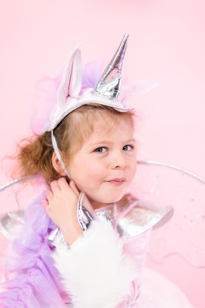 Porträt eines kleinen Mädchens im glitzernden Einhornkostüm auf rosa Hintergrund.