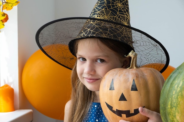 Porträt eines kleinen Mädchens im Hexenkostüm, das Kürbis mit Jack O Lantern-Gesicht zu Hause hält