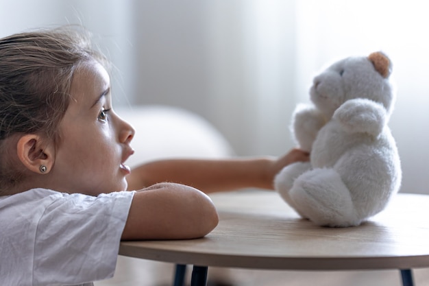 Porträt eines kleinen Mädchens mit einem Teddybären auf einem unscharfen Hintergrund im Inneren des Raumes.