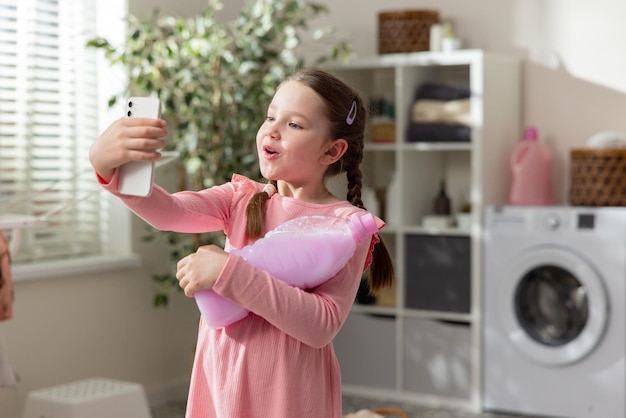 Porträt eines kleinen Mädchens mit Zöpfen, das ein rosafarbenes Kleid trägt. Kind hält Smartphone