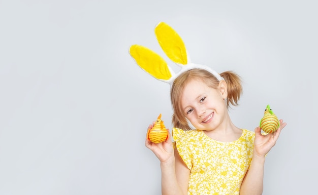 Porträt eines kleinen niedlichen kaukasischen lächelnden Mädchens mit Hasenohren und Dekorationen für Ostern in den Händen.