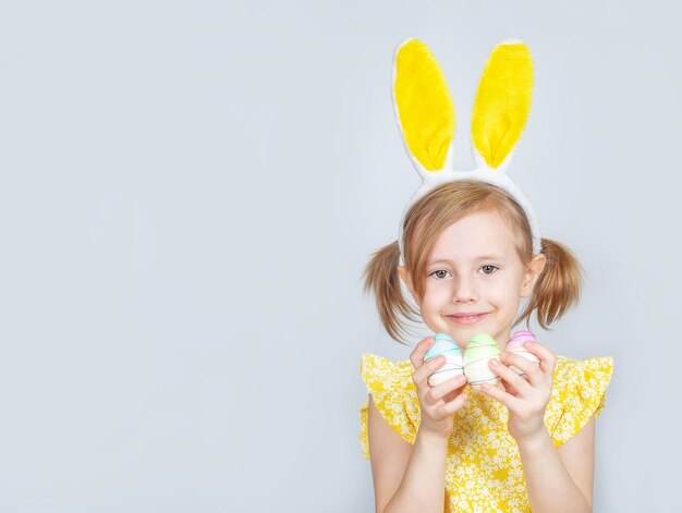 Porträt eines kleinen niedlichen kaukasischen lächelnden Mädchens mit Hasenohren und Dekorationen für Ostern in den Händen.