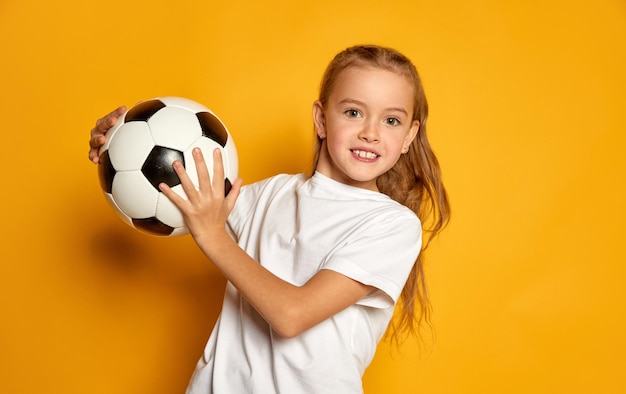 Porträt eines kleinen schönen Mädchens im weißen T-Shirt, das mit isoliertem Fußballball posiert