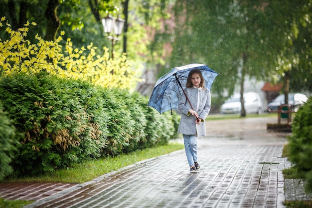 Porträt eines kleinen, schönen, stilvollen Mädchens mit einem Regenschirm im Regen im Stadtpark