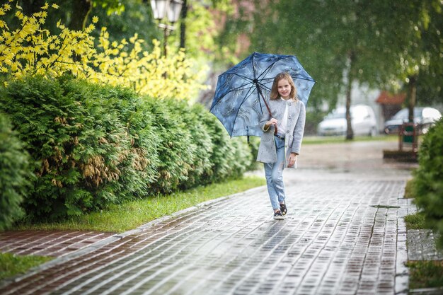 Porträt eines kleinen, schönen, stilvollen Mädchens mit einem Regenschirm im Regen im Stadtpark