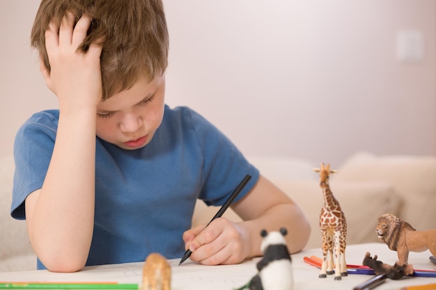 Porträt eines kleinen Schuljungen, der am Tisch sitzt und mit Farbfarbe zeichnet