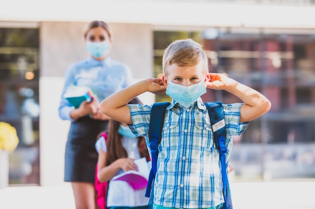 Porträt eines kleinen Schuljungen, der versucht, eine medizinische Maske auf seinem Gesicht zu befestigen