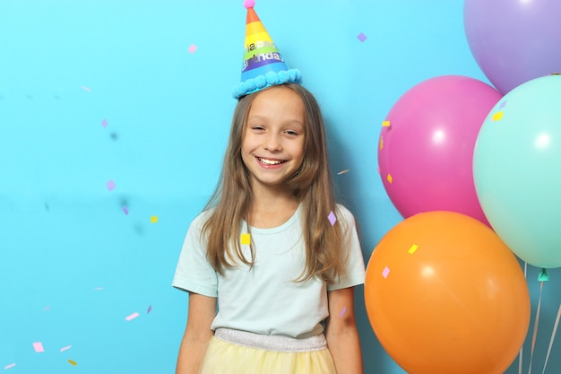 Porträt eines kleinen süßen Mädchens in einer festlichen Mütze und mit Luftballons