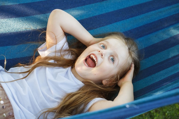 Porträt eines kleinen süßen Mädchens mit langen Haaren, das auf einer Hängematte im Garten ruht und lächelt