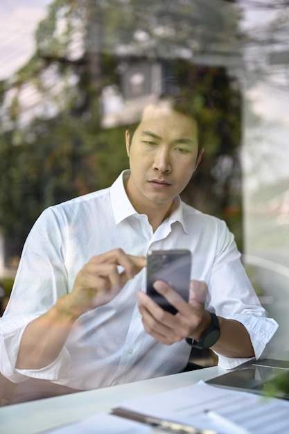 Porträt eines konzentrierten asiatischen Geschäftsmannes, der seine Nachrichten auf seinem Smartphone liest
