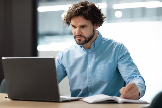 Porträt eines konzentrierten Mannes, der einen Laptop verwendet und in ein Notizbuch schreibt