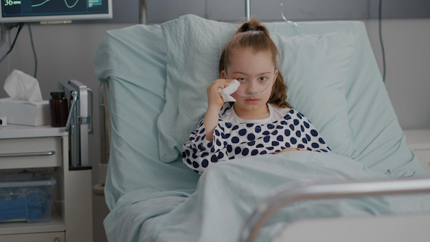 Porträt eines kranken, allein gefährdeten kleinen kindes, das beim weinen während der krankheitsuntersuchung in der krankenstation in die kamera schaut. im krankenhaus eingeliefertes kind, das nach einer genesungsoperation im bett ruht
