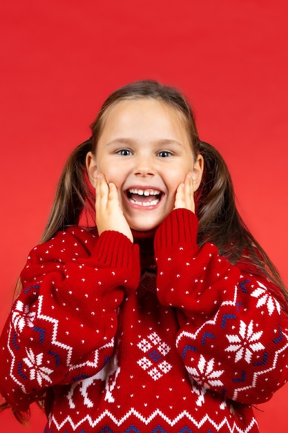 Porträt eines lachenden überraschten Mädchens in rotem Weihnachtspullover mit Rentier, das Gesicht mit Palmen berührt ...
