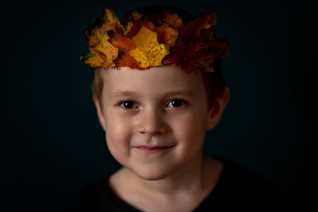 Porträt eines lächelnden 4-6-Kindes mit einer Blätterkrone auf dem Kopf an einer dunkelgrünen Wand