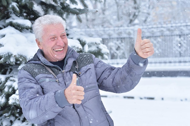 Porträt eines lächelnden älteren Mannes, der im Winter draußen steht und Daumen nach oben zeigt