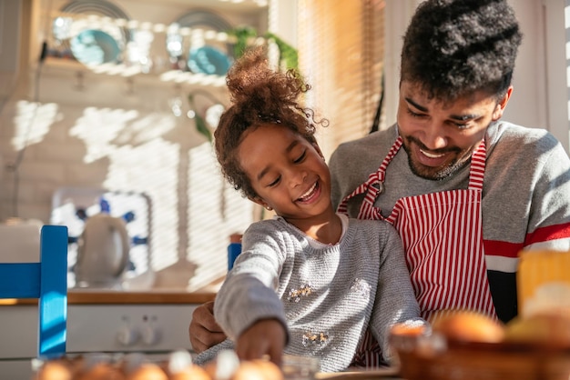 Porträt eines lächelnden afroamerikanischen Vaters und einer Tochter, die in der Küche backen.