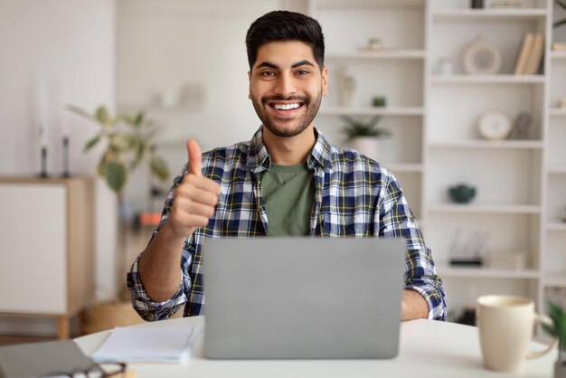 Porträt eines lächelnden arabischen Mannes mit Laptop, der Daumen nach oben zeigt