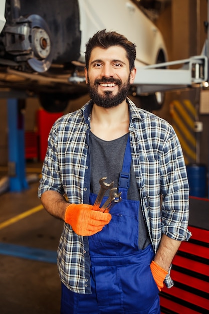 Porträt eines lächelnden Arbeiters im Auto-Service-Center, der Schraubenschlüssel hält und nach vorne schaut