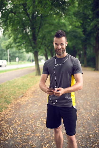 Porträt eines lächelnden Athleten, der Musik über ein Handy im Park hört