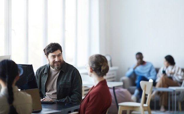 Porträt eines lächelnden bärtigen Mannes, der während eines Treffens im modernen Büro mit einer Kollegin spricht, Kopienraum