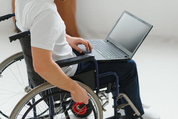 Porträt eines lächelnden behinderten Mannes, der im Rollstuhl sitzt und von zu Hause aus am Laptop arbeitet Junger Arbeitnehmer mit besonderen Bedürfnissen Konzept für Freiberufler und Menschen mit Behinderungen