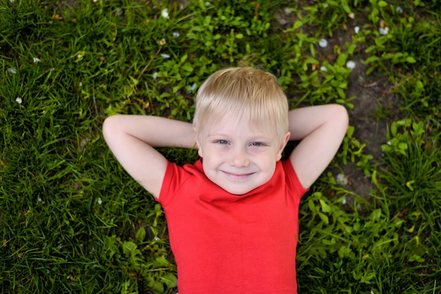 Porträt eines lächelnden blonden Jungen, der auf dem Gras liegt