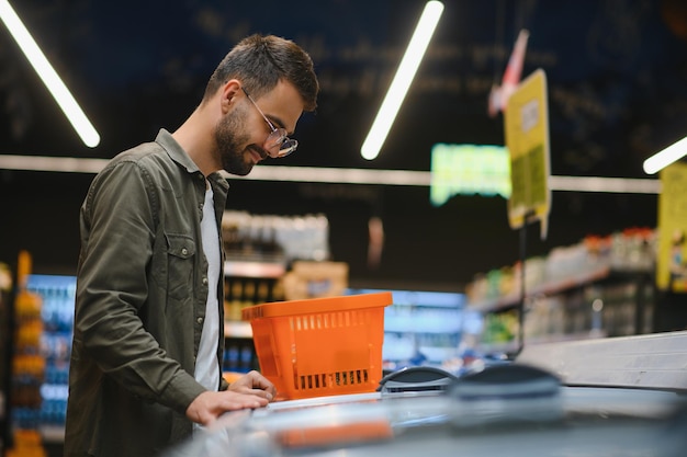 Foto porträt eines lächelnden, gutaussehenden mannes, der im supermarkt lebensmittel einkauft und lebensmittel aus dem regal auswählt