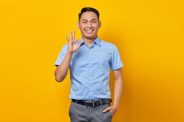 Porträt eines lächelnden jungen asiatischen Mannes mit Brille, der ein Okay-Zeichen zeigt, das auf gelbem Hintergrund isoliert ist Geschäftsmann- und Unternehmerkonzept