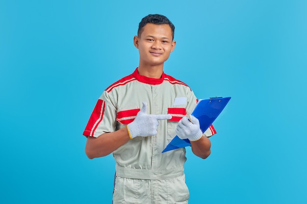 Porträt eines lächelnden jungen asiatischen Mechanikers, der mit dem Finger auf blauem Hintergrund auf die Zwischenablage zeigt