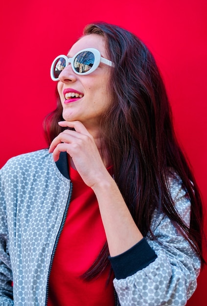 Porträt eines lächelnden jungen Brunettemädchens mit Sonnenbrille auf flachem rotem Hintergrund red