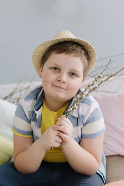 Porträt eines lächelnden Jungen in einem Hut, der Weidenzweige hält