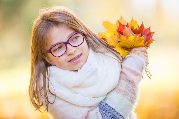 Porträt eines lächelnden jungen Mädchens, das in der Hand einen Strauß herbstlicher Ahornblätter hält