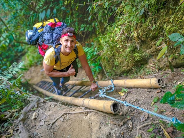 Porträt eines lächelnden jungen Mannes, der eine Leiter im Wald erklimmt