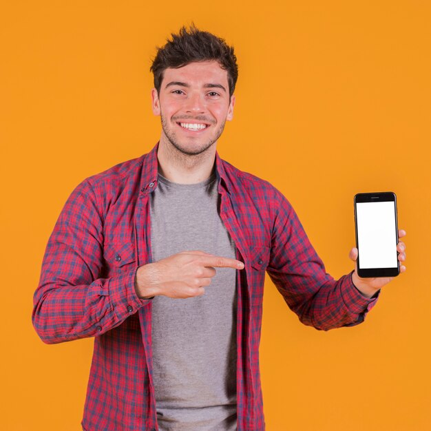 Porträt eines lächelnden jungen Mannes, der seinen Handy gegen einen orange Hintergrund zeigt