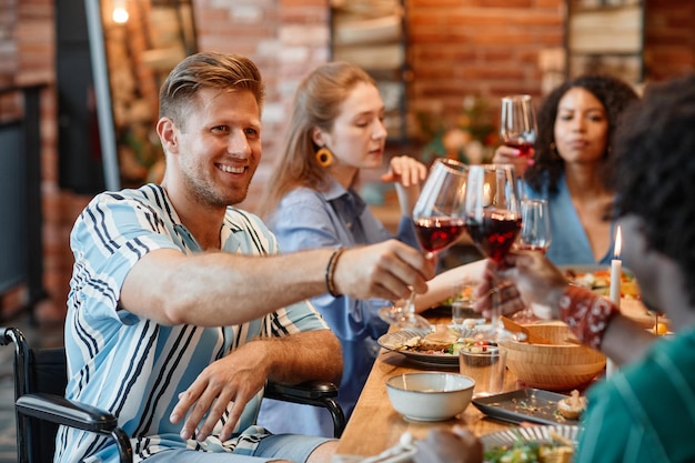 Porträt eines lächelnden jungen Mannes mit Behinderung, der während der Dinnerparty mit Freunden anstößt