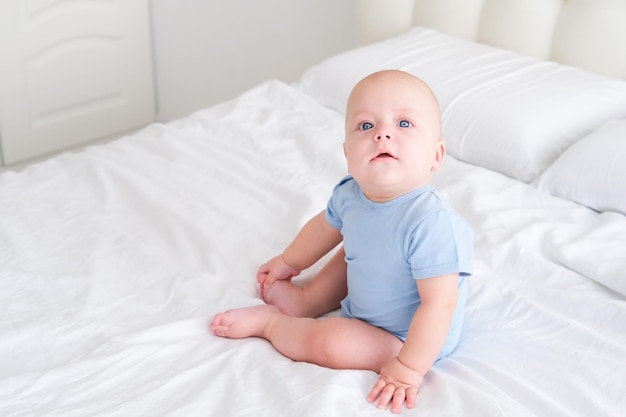 Porträt eines lächelnden Jungen mit großen blauen Augen im Bodysuit auf weißer Bettwäsche. Gesundes neugeborenes Kind