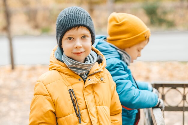 Porträt eines lächelnden Jungen mit Hut und gelber Jacke, auf der Straße. Gehen Sie im Herbst auf die Straße. Hübscher und süßer Junge, der in den Rahmen schaut, lächelt