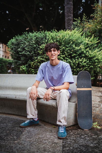 Porträt eines lächelnden jungen Skater-Mannes, der in die Kamera schaut Er sitzt auf einer Betonbank