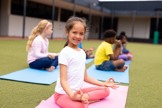 Porträt eines lächelnden kaukasischen Mädchens, das mit der Klasse im Freien Meditation übt