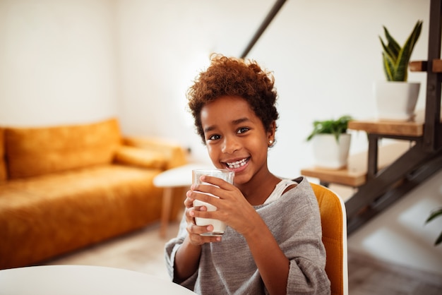 Porträt eines lächelnden kleinen Afroamerikanermädchens mit einem Glas Milch zu Hause.