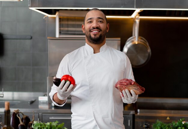 Foto porträt eines lächelnden koch mit fleisch und gemüse in der küche