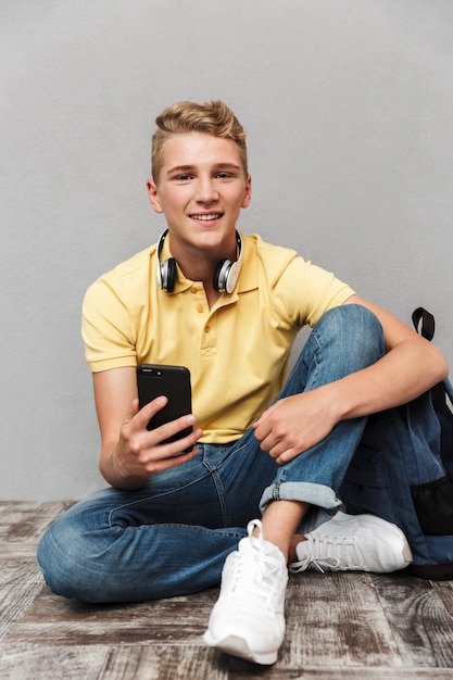 Porträt eines lächelnden lässigen Teenagers mit dem sitzenden Rucksack